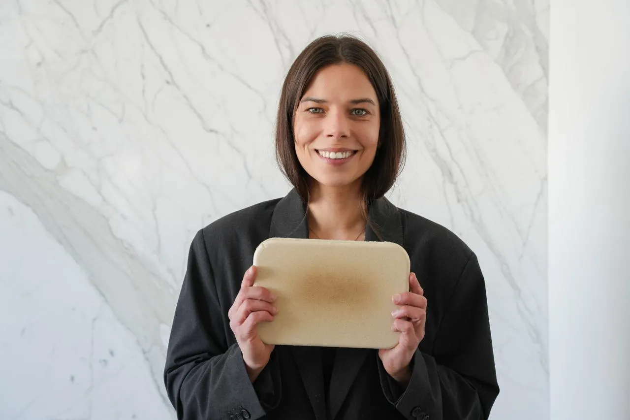 Jeanne Beck, Gründerin von Plant Plast, hält eine Platte aus Plant Plast mit sichtbarer Hanfschäben-Struktur in die Kamera